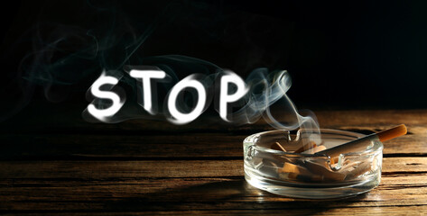 Quit smoking. Word Stop of smoke, ashtray with stubs and smoldering cigarette on wooden table...