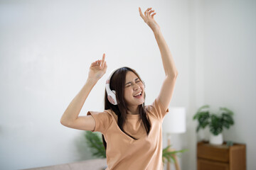 Happy Young Asian woman wearing headphone have fun and dancing listening to music relax in living room. beautiful joyful woman dancing in house