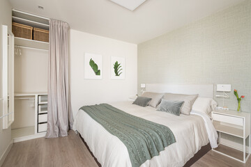 Stylish bright bedroom with a bedside table and a double bed and an empty wardrobe for things with beige wallpaper and cute pictures on the wall. The concept of an apartment for a young family
