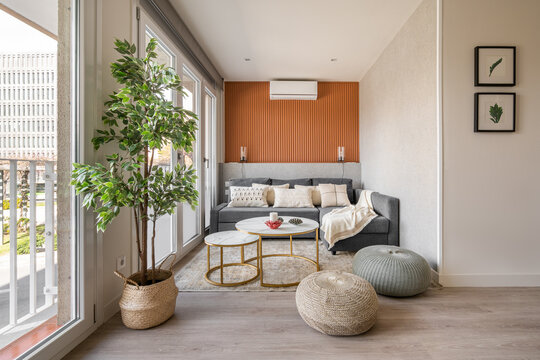 Stylish seating area with a terracotta color wall with a sofa and pouffes near the panoramic windows in the living room. The concept of a modern Scandinavian interior