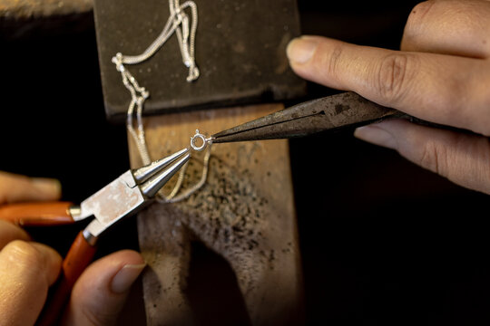 Close up of hands of biracial female worker making jewellery using tools at jewellery workshop - Powered by Adobe