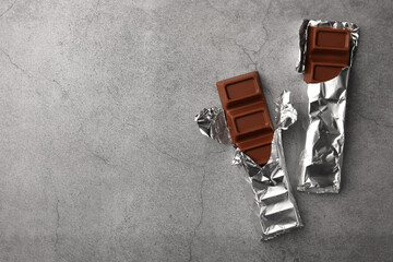 Tasty chocolate bars wrapped in foil on grey table, flat lay. Space for text