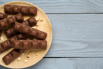 Plate of tasty chocolate bars and nuts on grey wooden table, top view. Space for text