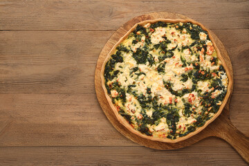 Delicious homemade spinach quiche on wooden table, top view. Space for text