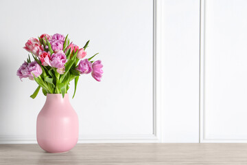 Beautiful bouquet of colorful tulip flowers on floor near white wall, space for text