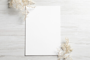Empty sheet of paper and gypsophila flowers on white wooden table, flat lay. Mockup for design
