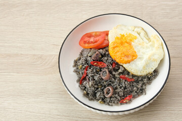 Nasi Goreng Cumi Hitam or Black Squid Fried Rice, served in white plate on wooden table
