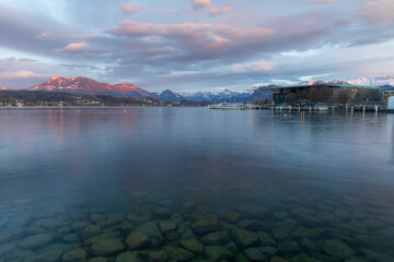 Beautiful landscape of Luzern lake in Switzerland with swiss alps snow cap mountain background in winter.Smooth water and space stone or rock foreground.Tourist travels in Europe.Twilight sky. 