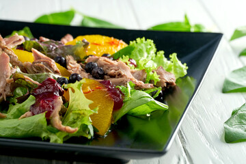Salad with baked duck, citrus fruits and berries in a black plate on a white background