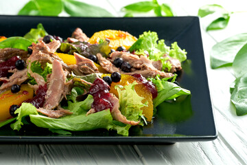 Salad with baked duck, citrus fruits and berries in a black plate on a white background