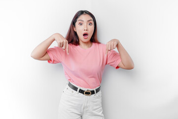 Obraz na płótnie Canvas Shocked Asian woman is wearing pink t-shirt, pointing at the copy space below her, isolated by white background