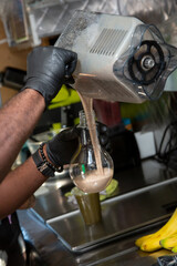 A view of hands pouring smoothie contents from a blender pitcher into a light bulb shaped drink cup.