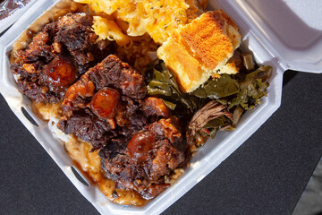 A top down view of an entree of smothered oxtails, with a side of mac n cheese, corn bread, and...