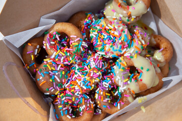 A top down view of a box of mini donuts, featuring rainbow sprinkles and icing.