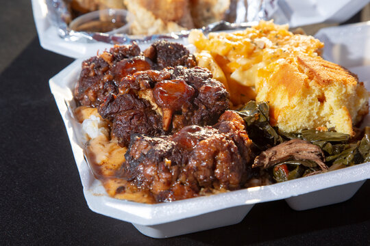 A view of an entree of smothered oxtails, with a side of mac n cheese, corn bread, and collard greens.