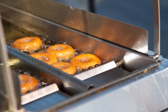 A view of some mini donuts being deep fried inside a small commercial automated donut making machine.