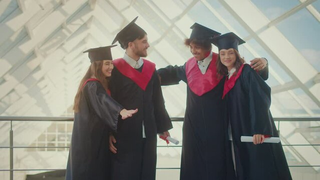 Portrait of Positive Group of four Graduates With Diplomas Hugging Together in Hallway of a University Building. Alumni of Educational institutions. Concept of Future Leaders