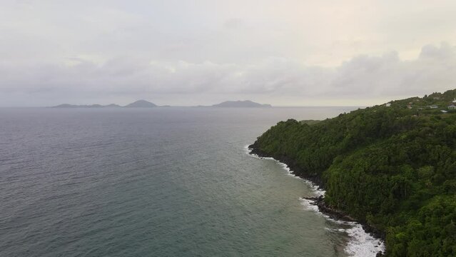 Immense sea next to island with trees,  clouds in the background on a cloudy day. Aerial drone shot.