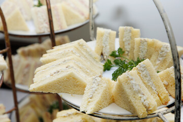 A view of food tier stands, featuring tuna salad tea sandwiches.
