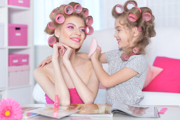 Obraz na płótnie Canvas Happy mother and little daughter with hair curlers at home reading magazine