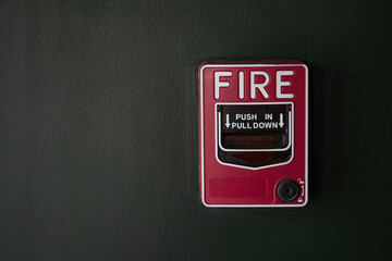 Red emergency fire alarm switch at the black cement wall inside the office for fire protection