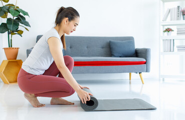 Fototapeta premium Asian beautiful healthy fit slim sexy female sporty athlete model in sportswear and leggings sitting bending head down rolling yoga mat out ready for workout exercising training in living room