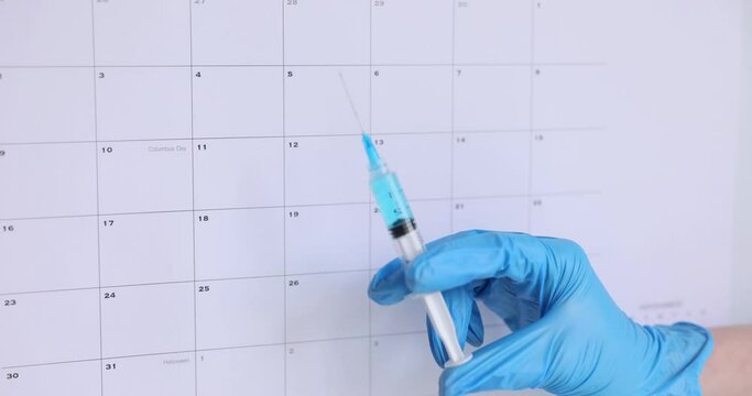 Doctor hand in protective glove holds syringe with medical liquid. Therapist checks calendar preparing patient for vaccination. Healthcare concept