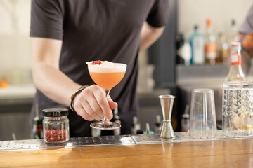 Hand of bartender serving fresh red summer fruit cocktail at bar counter on sunny day.