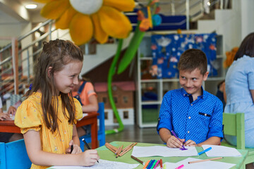 Cute girl and boy sit and draw together in preschool institution