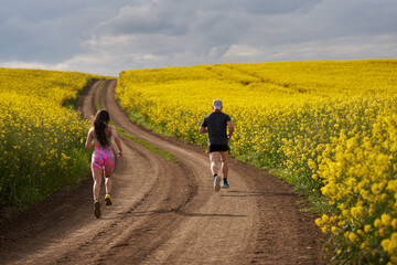 Fototapeta premium Endurance runners on a dirt track in a canola field, training
