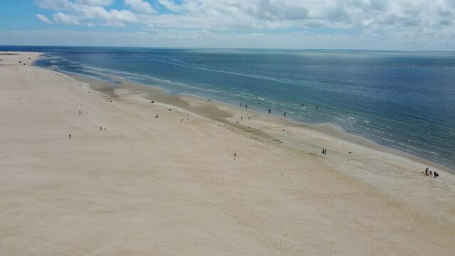 People play and relax on wide spread of golden sand and calm ocean in Denmark, sonderstrand beach aerial