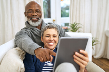 Technology, senior couple with tablet and on sofa happy in living room of their home. Social media or streaming, retirement or relax and happy married people on couch laughing with digital device