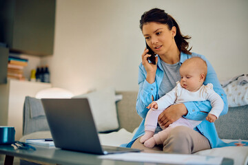 Busy mother talks on cell phone while babysitting her daughter and working at home.