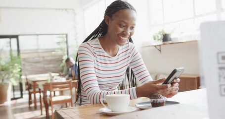 Happy african american woman using smartphone at coffee shop, slow motion