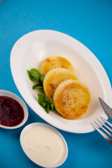 Round cottage cheese pancakes in a white plate on a blue background. Food breakfast. Healthy food.