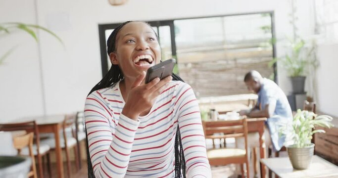 Happy african american woman talking on smartphone at coffee shop, slow motion