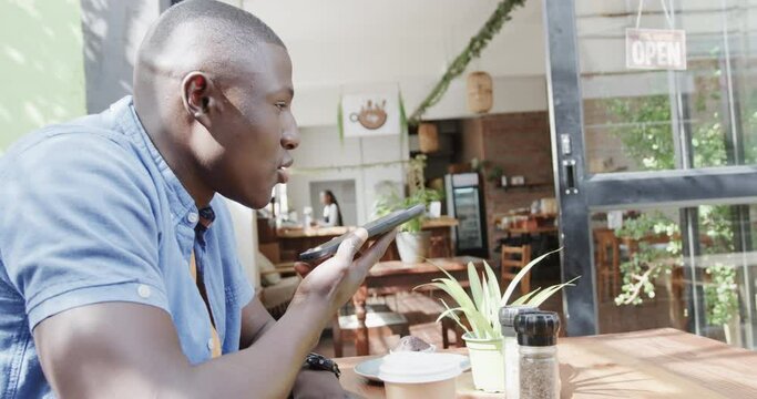 Happy african american man talking on smartphone at coffee shop, slow motion