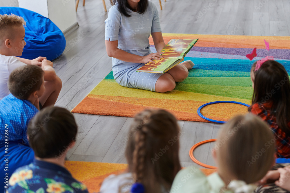 Wall mural reading time in an elementary school or kindergarten, a teacher reading a book to children in an ele