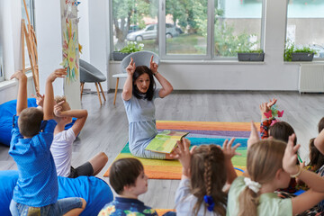 Fototapeta premium A happy female teacher sitting and playing hand games with a group of little schoolchildren