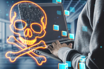 Side view of hacker using laptop with glowing digital binary code skull on blurry office interior background. Hacking, piracy, malware and data theft concept. Double exposure.