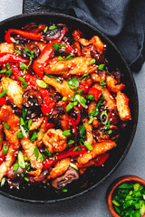 Asian cuisine, stir fry with chicken fillet, red paprika, mushrooms green onion and sesame in frying pan. Gray kitchen table background, top view, copy space