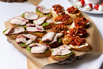 A Variety of Appetizing Bruschetta. A colorful variety of freshly-crafted bruschetta appetizers made with fried vegetables, turkey breast meat, pesto sauce spread and bread, served on wooden board.