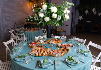 Wedding reception table with different food and drinks. A festive banquet setting featuring a variety of food and drinks, fresh flowers, and decorations for celebrating a  special occasion.