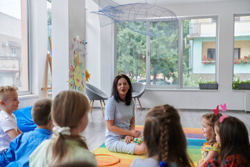 A happy female teacher sitting and playing hand games with a group of little schoolchildren