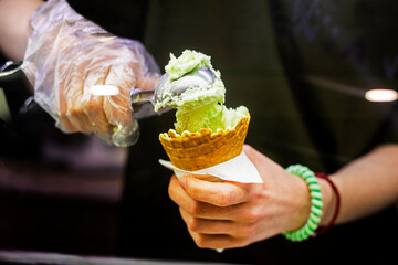 seller in disposable gloves put pistachio ice cream in a waffle cup.