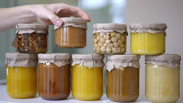 Delicious canned honey and nuts in bottles with female hand placing jar on row up. Unrecognizable young Caucasian woman putting tasty sweet dessert for sale on shelf