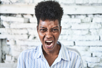 A miggle-aged african woman sitting on her sofa screaming very angry and aggressive. - obrazy, fototapety, plakaty