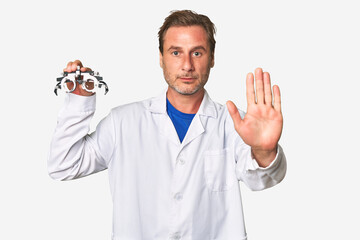 A middle-aged optometrist man standing with outstretched hand showing stop sign, preventing you.