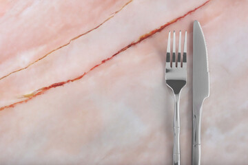 Shiny fork and knife on pink marble table, flat lay. Space for text