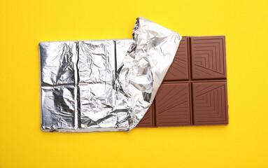 Tasty chocolate bar on yellow background, top view
